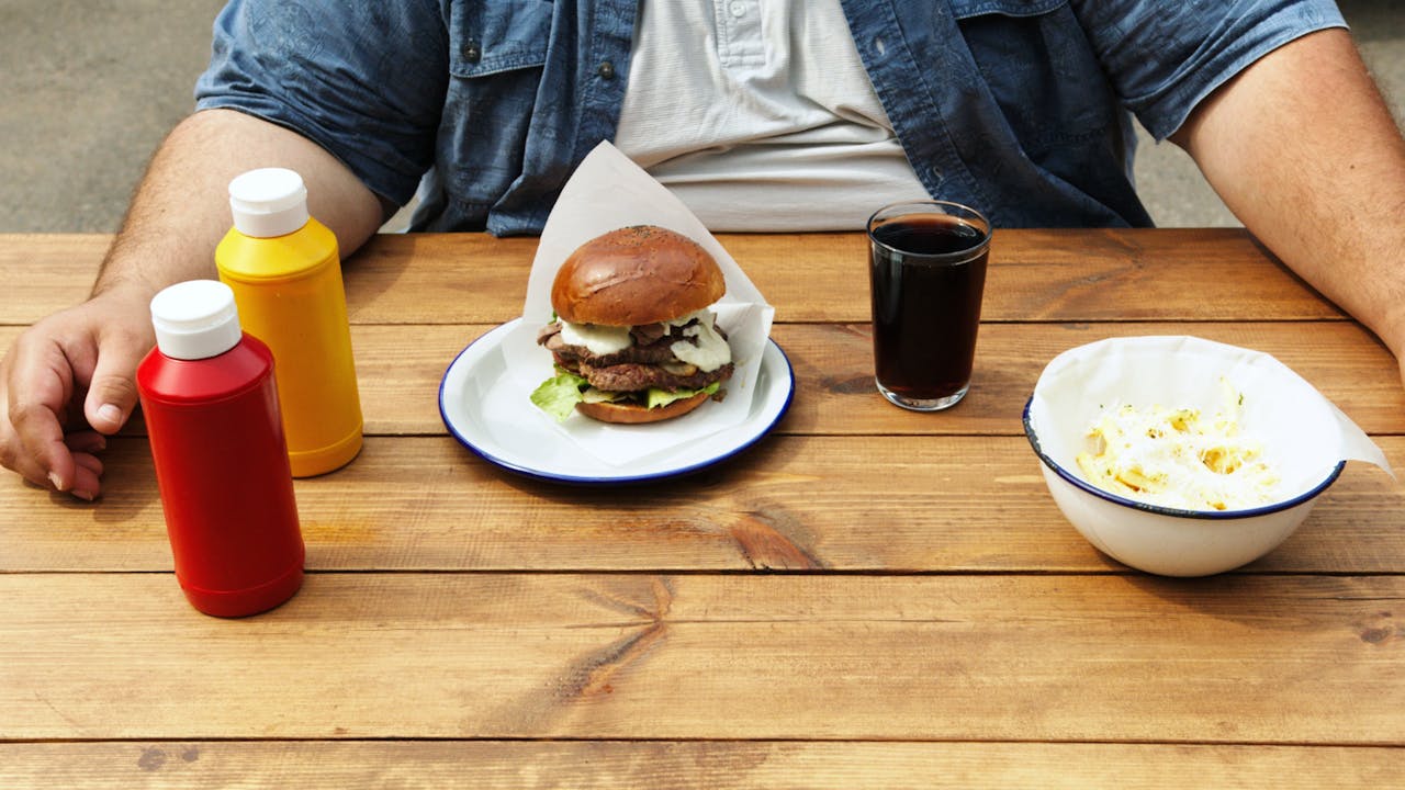 Casual dining with a burger, soda, and sauces at outdoor table. Perfect for summer vibes.